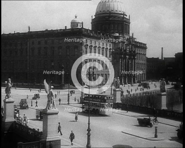 Bus Driving Down a Wide Road with a Large Building in the Background, 1933. Creator: British Pathe Ltd.