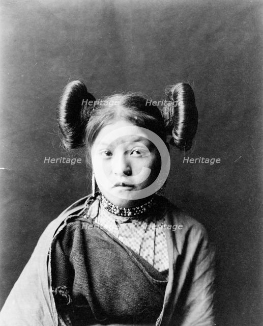 Gobuguoy, Walpi girl, half-length portrait, facing front, hair tied in swirls on sides of..., c1900. Creator: Edward Sheriff Curtis.