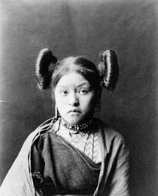 Gobuguoy, Walpi girl, half-length portrait, facing front, hair tied in swirls on sides of..., c1900. Creator: Edward Sheriff Curtis