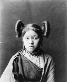 Gobuguoy, Walpi girl, half-length portrait, facing front, hair tied in swirls on sides of..., c1900. Creator: Edward Sheriff Curtis