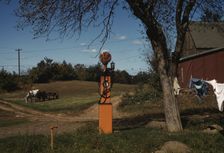 Gas pump with clothesline, barn and horse-drawn wagon in background, between 1941 and 1942. Creator: Unknown