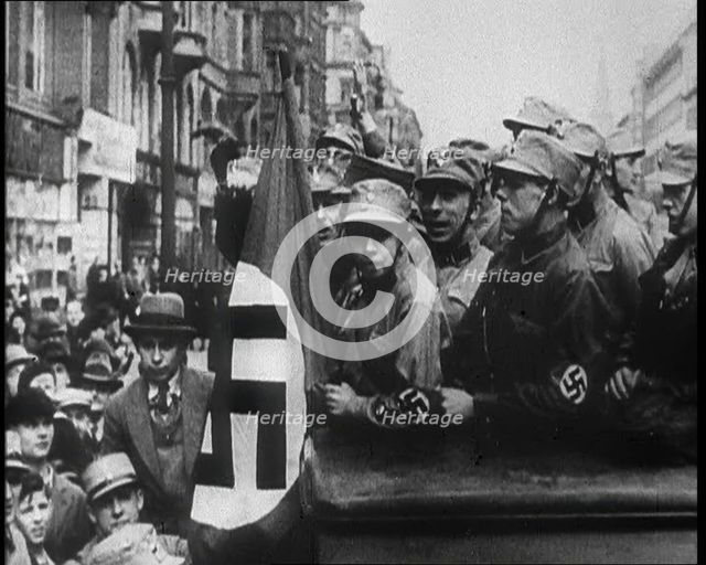German Civilians and Men in Nazi Uniforms With a Nazi Flag, 1933. Creator: British Pathe Ltd.