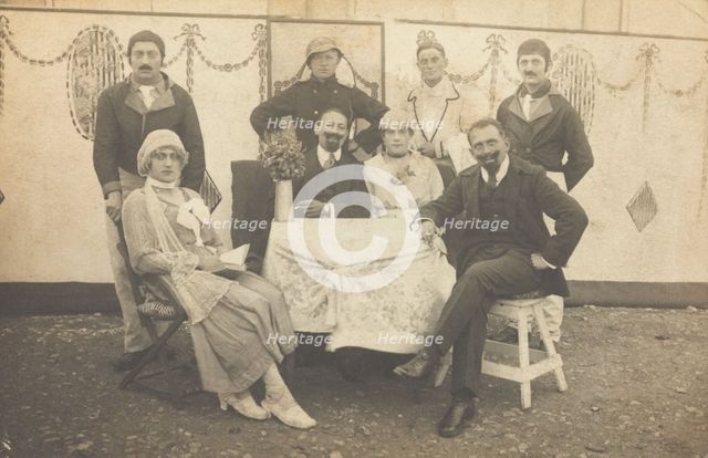 German soldiers, some in drag, pose round a table at a concert party, (between 1910 and 1919?). Creator: Unknown.