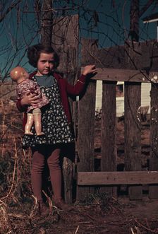 Girl with doll standing by fence, between 1941 and 1942. Creator: Unknown