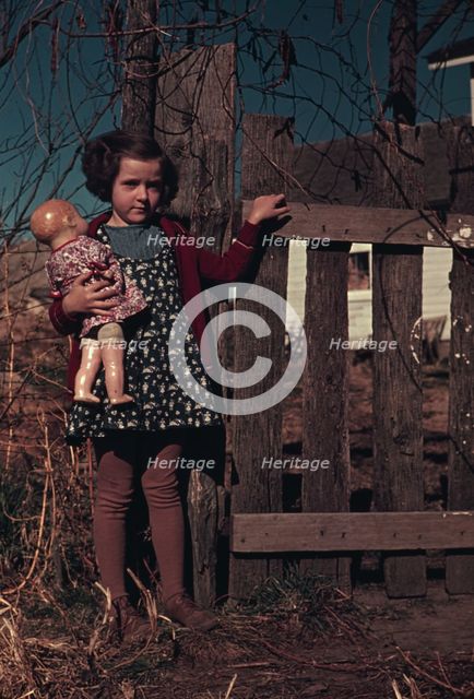 Girl with doll standing by fence, between 1941 and 1942. Creator: Unknown.