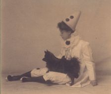 Girl dressed in a pierrot costume with a small black dog on her lap, between 1900 and 1920. Creator: Unknown