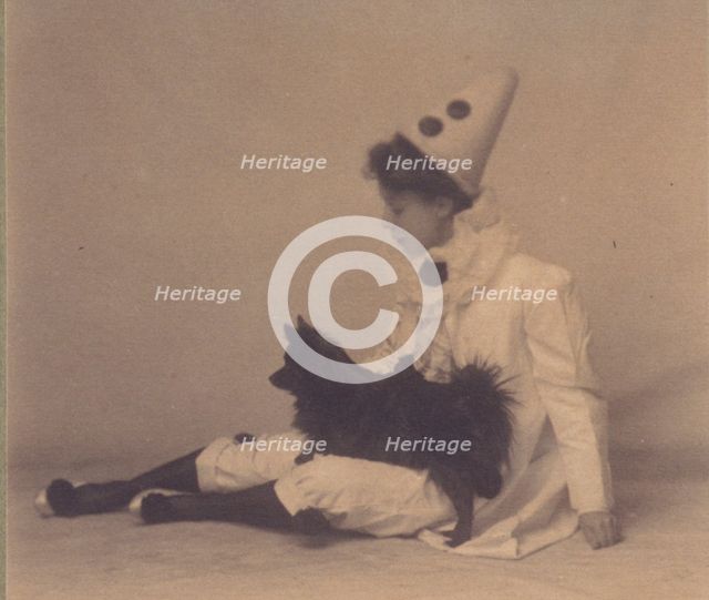Girl dressed in a pierrot costume with a small black dog on her lap, between 1900 and 1920. Creator: Unknown.