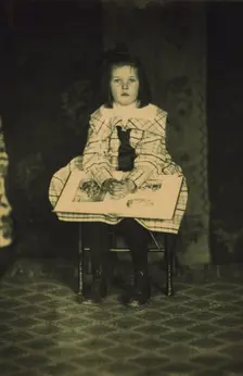 Girl in a plaid dress seated with a book in her lap, c1900. Creator: Mathilde Weil