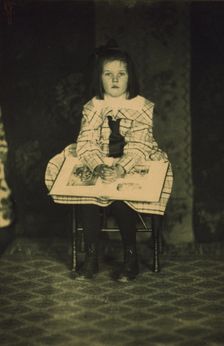 Girl in a plaid dress seated with a book in her lap, c1900. Creator: Mathilde Weil