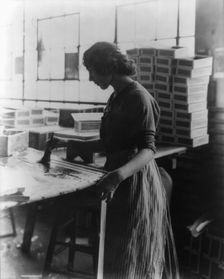 Girl painting strips with glue to assemble cigar boxes, c1910. Creator: Frances Benjamin Johnston