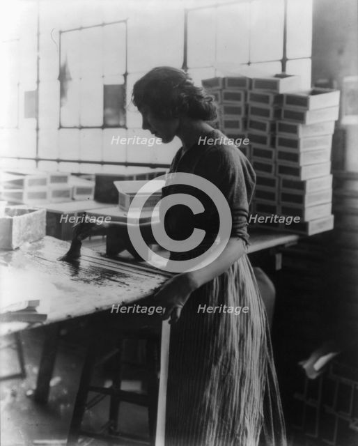Girl painting strips with glue to assemble cigar boxes, c1910. Creator: Frances Benjamin Johnston.