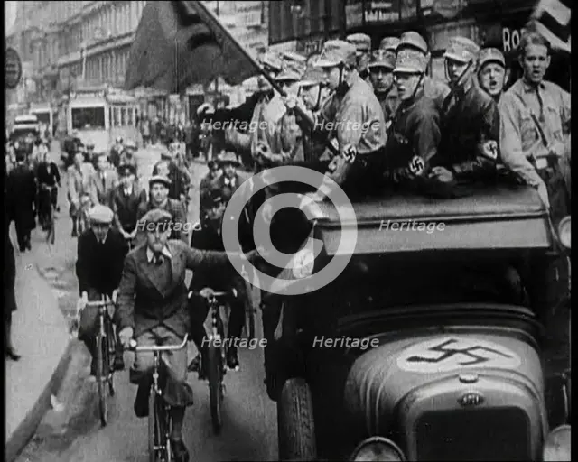 Group of Men in Nazi Uniform Driving Down the Road as Civilians Watch, 1933. Creator: British Pathe Ltd.