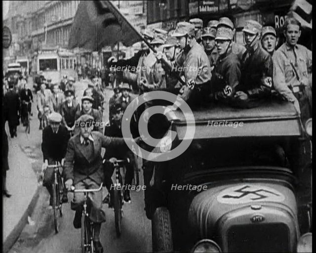 Group of Men in Nazi Uniform Driving Down the Road as Civilians Watch, 1933. Creator: British Pathe Ltd.