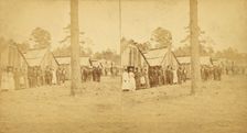 Group lined up in front of a row of shacks, (1868-1900?). Creator: Unknown