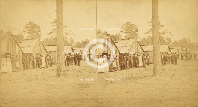 Group lined up in front of a row of shacks, (1868-1900?). Creator: Unknown.