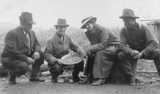 Group portrait of a woman and three men, crouched outside, smiling; one..., between c1900 and 1916. Creator: Unknown