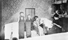 Domestic scene showing a mother with her children finishing trousers, London, c1900. Creator: Unknown
