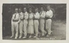 Entertainers, one in drag, pose in a line in front of foliage, [between 1910 and 1919?]. Creator: Unknown