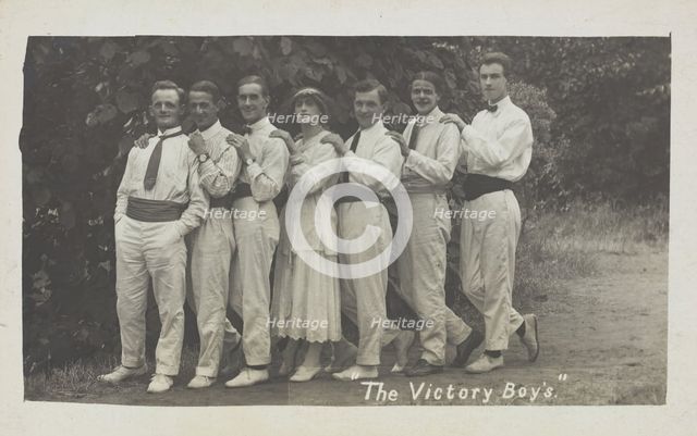Entertainers, one in drag, pose in a line in front of foliage, [between 1910 and 1919?]. Creator: Unknown.