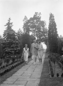 Edge, Charles N., walking with Margaret Edge and another woman in his garden, 1932 or 1933. Creator: Arnold Genthe