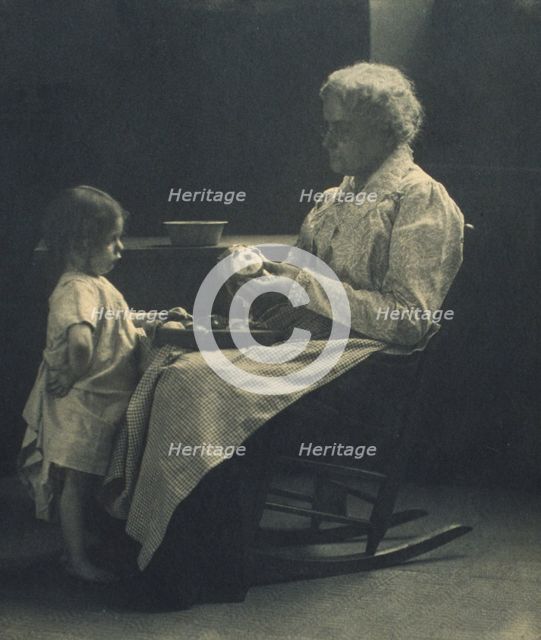 Elderly woman in a rocking chair peeling apple with young girl standing in front of her, c1900. Creator: Elizabeth B. Brownell.