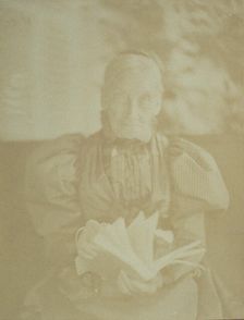 Elderly woman sitting in a chair holding a book, half-length portrait, facing front, c1890. Creator: Horace L Bundy