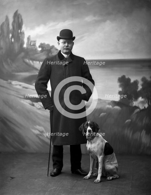 Elegant man wearing a black overcoat posing with his dog, Landskrona, Sweden, 1910. Creator: Unknown.