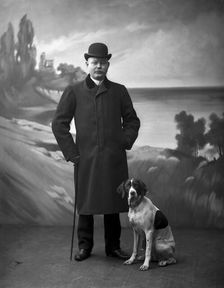 Elegant man wearing a black overcoat posing with his dog, Landskrona, Sweden, 1910