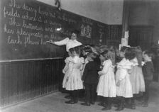 Elementary school children standing and watching teacher write at blackboard, Washington DC, (1899?) Creator: Frances Benjamin Johnston