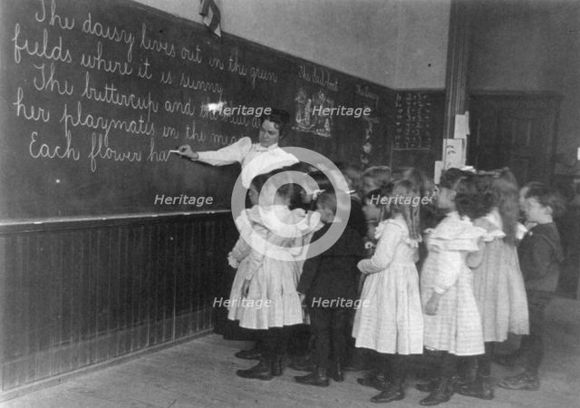 Elementary school children standing and watching teacher write at blackboard, Washington DC, (1899?) Creator: Frances Benjamin Johnston.