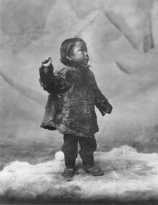 Eskimo child posing while standing on fur rug, between c1900 and c1930. Creator: Unknown