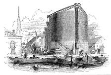 Exterior view of City of London Gasworks, showing gasometers and coal barges at the quay, 1876