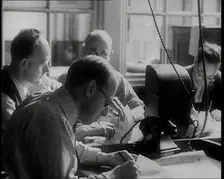 Four Male British Journalists Sitting Around a Table Covered in Papers and Writing, 1939. Creator: British Pathe Ltd