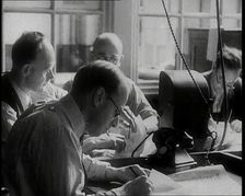 Four Male British Journalists Sitting Around a Table Covered in Papers and Writing, 1939. Creator: British Pathe Ltd