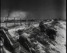 Four Male German Army Soldiers Lying Low on a Slope Below a Fence While Columns of Smoke..., 1939. Creator: British Pathe Ltd