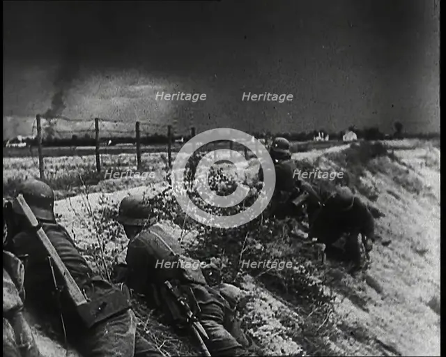Four Male German Army Soldiers Lying Low on a Slope Below a Fence While Columns of Smoke..., 1939. Creator: British Pathe Ltd.