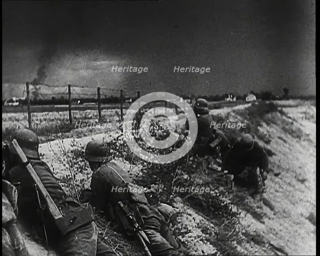 Four Male German Army Soldiers Lying Low on a Slope Below a Fence While Columns of Smoke..., 1939. Creator: British Pathe Ltd.