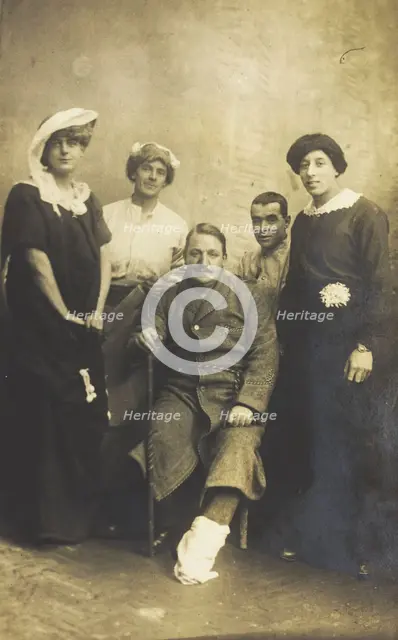 Four soldiers posing, three in drag, with an injured soldier seated in the centre, [1910-1919?]. Creator: Unknown.