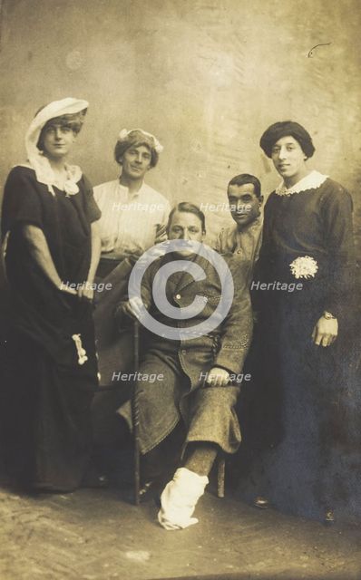 Four soldiers posing, three in drag, with an injured soldier seated in the centre, [1910-1919?]. Creator: Unknown.