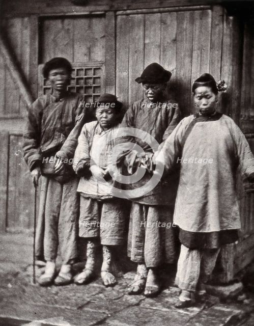 Foochow, China: four people with leprosy, wearing thick clothing, standing outside a wooden..., 1873 Creator: John Thomson.