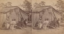 Family group sitting in front of a wooden shack, (1868-1900?). Creator: Unknown