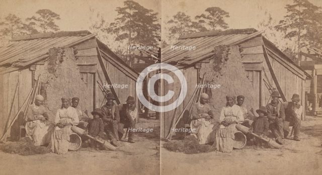 Family group sitting in front of a wooden shack, (1868-1900?). Creator: Unknown.