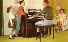 Family singing around a Wurlitizer organ as father plays, De Kalb, Illinois, USA, 1962