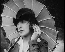 Fashionable Lady Sitting in a Garden Wearing Headphones and Carrying a Parasol, 1922. Creator: British Pathe Ltd