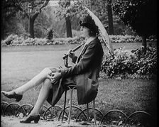 Fashionable Lady Sitting in a Garden Wearing Headphones and Carrying a Parasol, 1922. Creator: British Pathe Ltd
