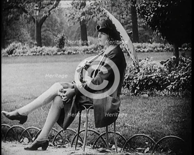 Fashionable Lady Sitting in a Garden Wearing Headphones and Carrying a Parasol, 1922. Creator: British Pathe Ltd.