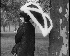 Female Civilian Dressed Glamorously Holding a Fur Trimmed Parasol in a Park, 1920. Creator: British Pathe Ltd