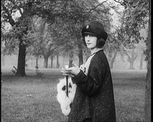 Female Civilian Dressed Glamorously Holding a Fur Trimmed Parasol in a Park, 1920. Creator: British Pathe Ltd