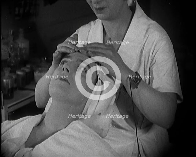 Female Civilian Having Her Face Massaged by Another Female Civilian Wearing an Electric, ... 1920. Creator: British Pathe Ltd.