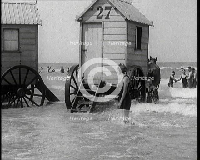 Female Civilian in Bathing Suit Standing in the Sea Watching Changing Cabins on Wheels Being...,1924 Creator: British Pathe Ltd.